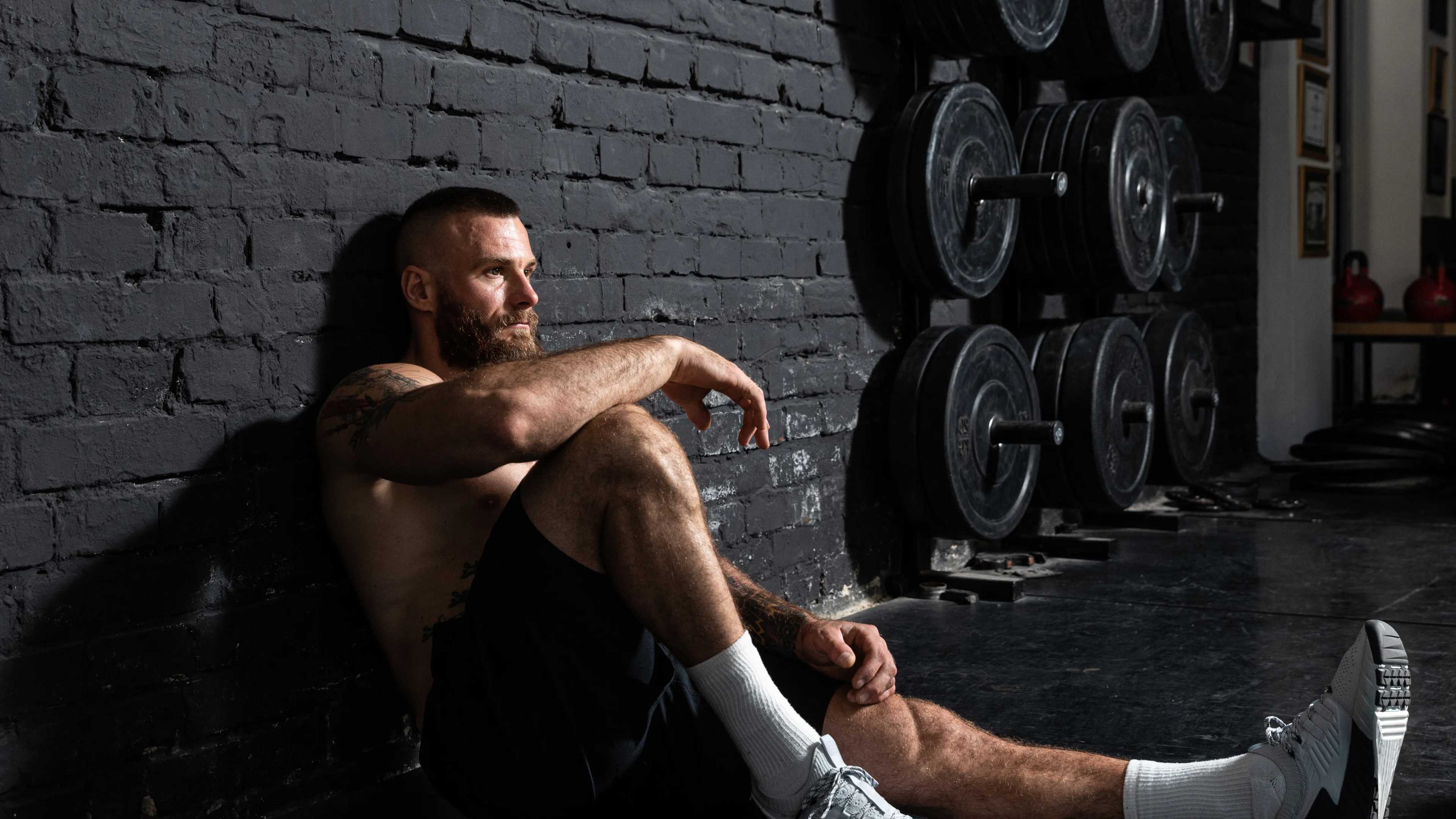Ein Mann sitzt erschöpft auf dem Boden eines Fitnessstudios