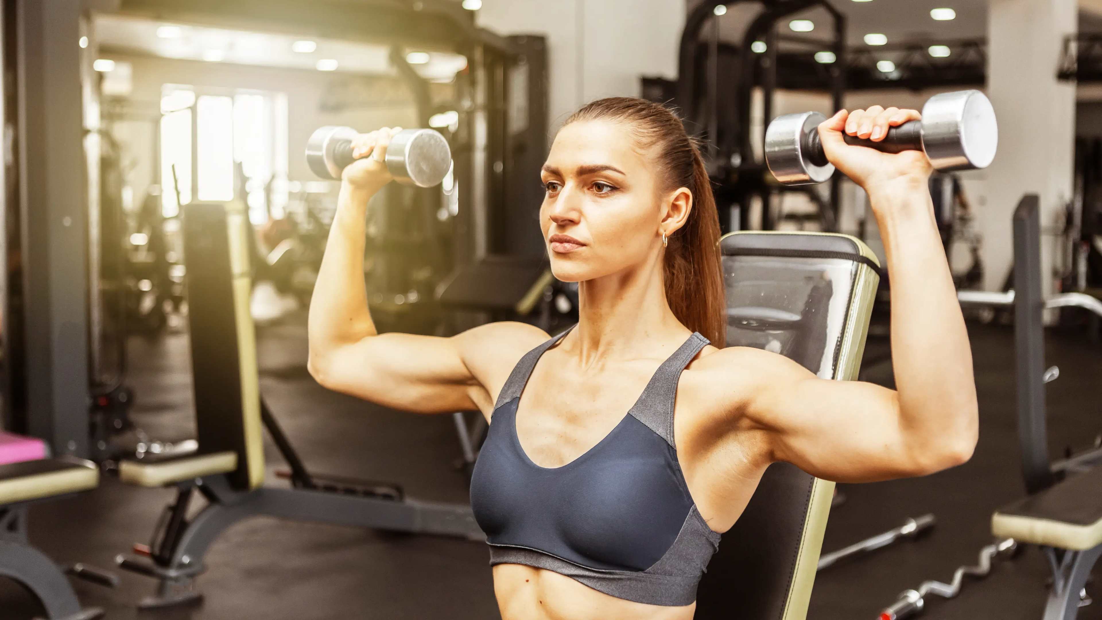 Eine Frau beim Kurzhantel-Schulterdrücken im Fitnessstudio