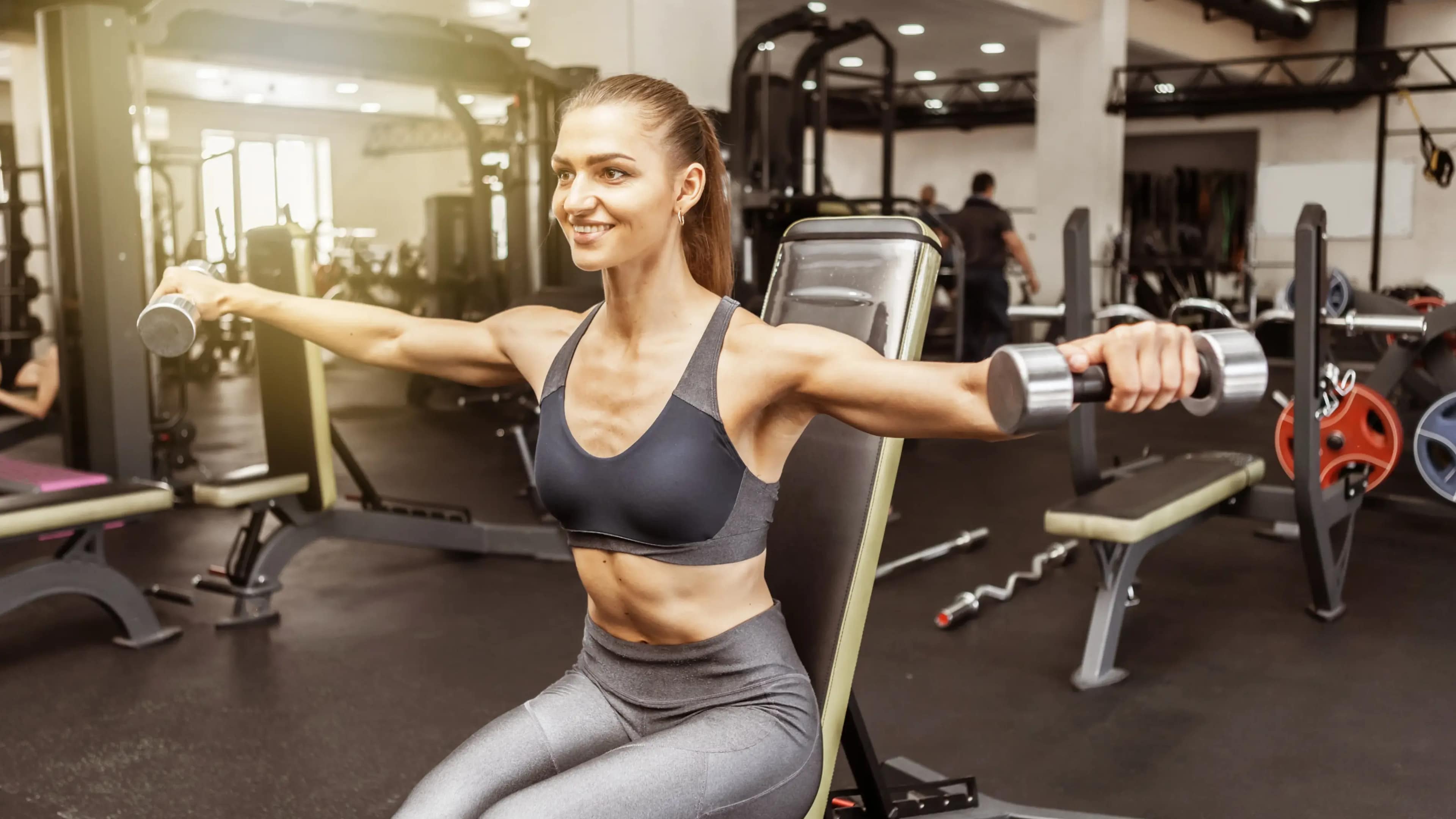 Eine Frau beim Seitheben mit Kurzhanteln im Fitnessstudio
