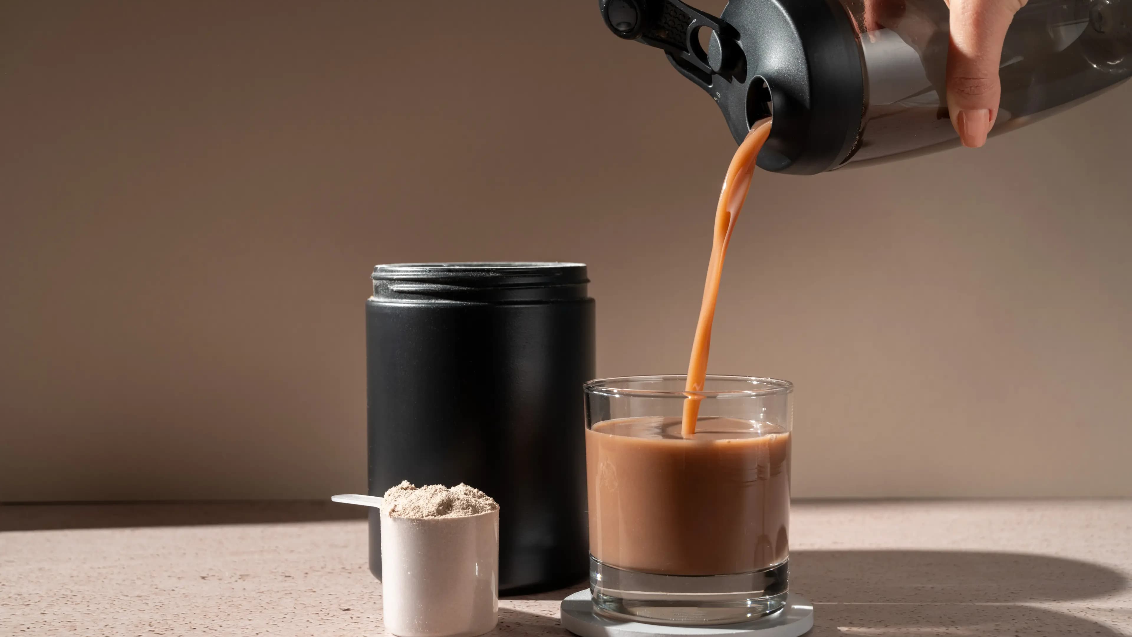 Eine Hand gießt ein Getränk aus einem Shaker in ein Glas ein