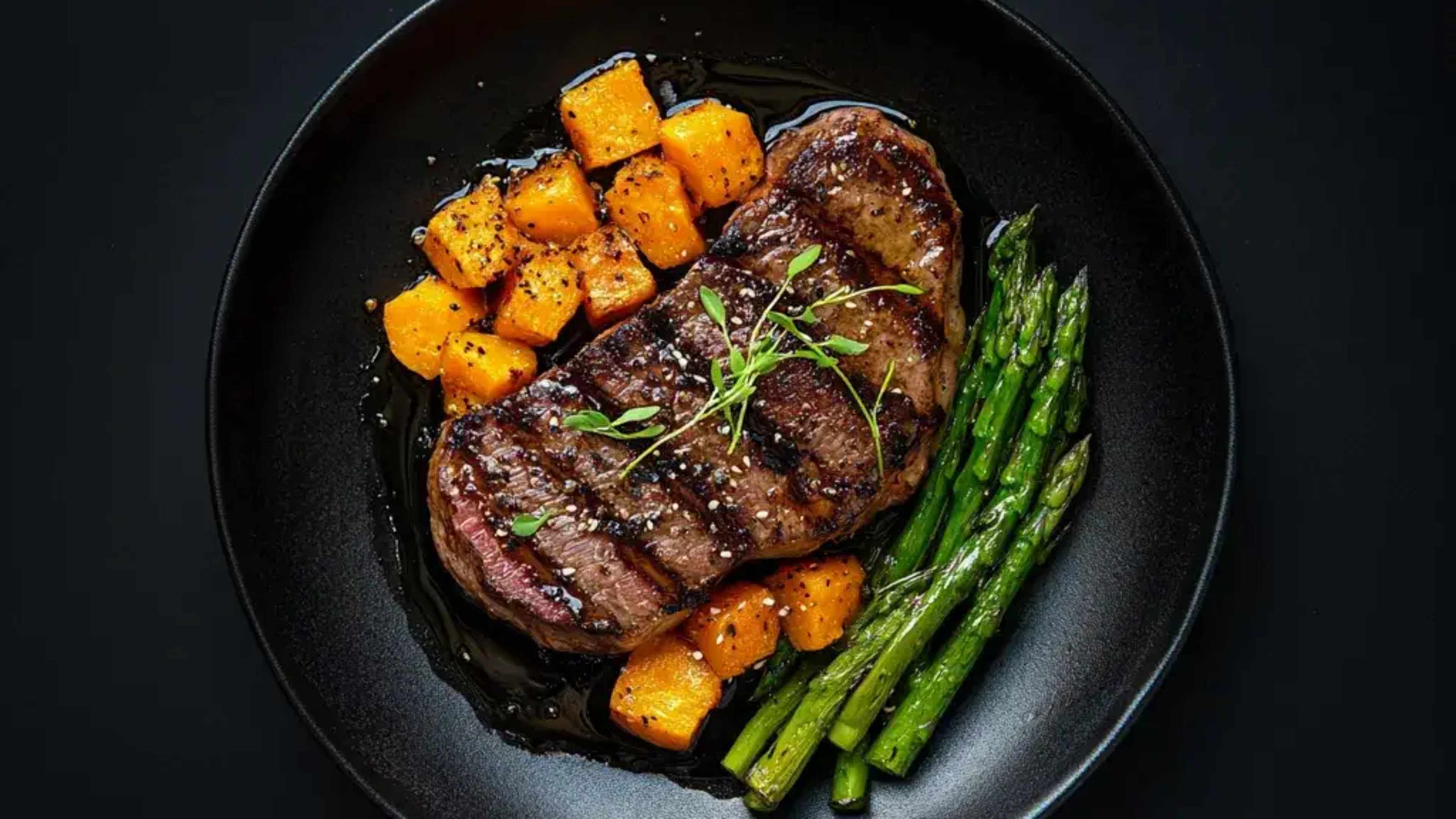 Steak mit Süßkartoffel und Spargel auf einem schwarzen Teller