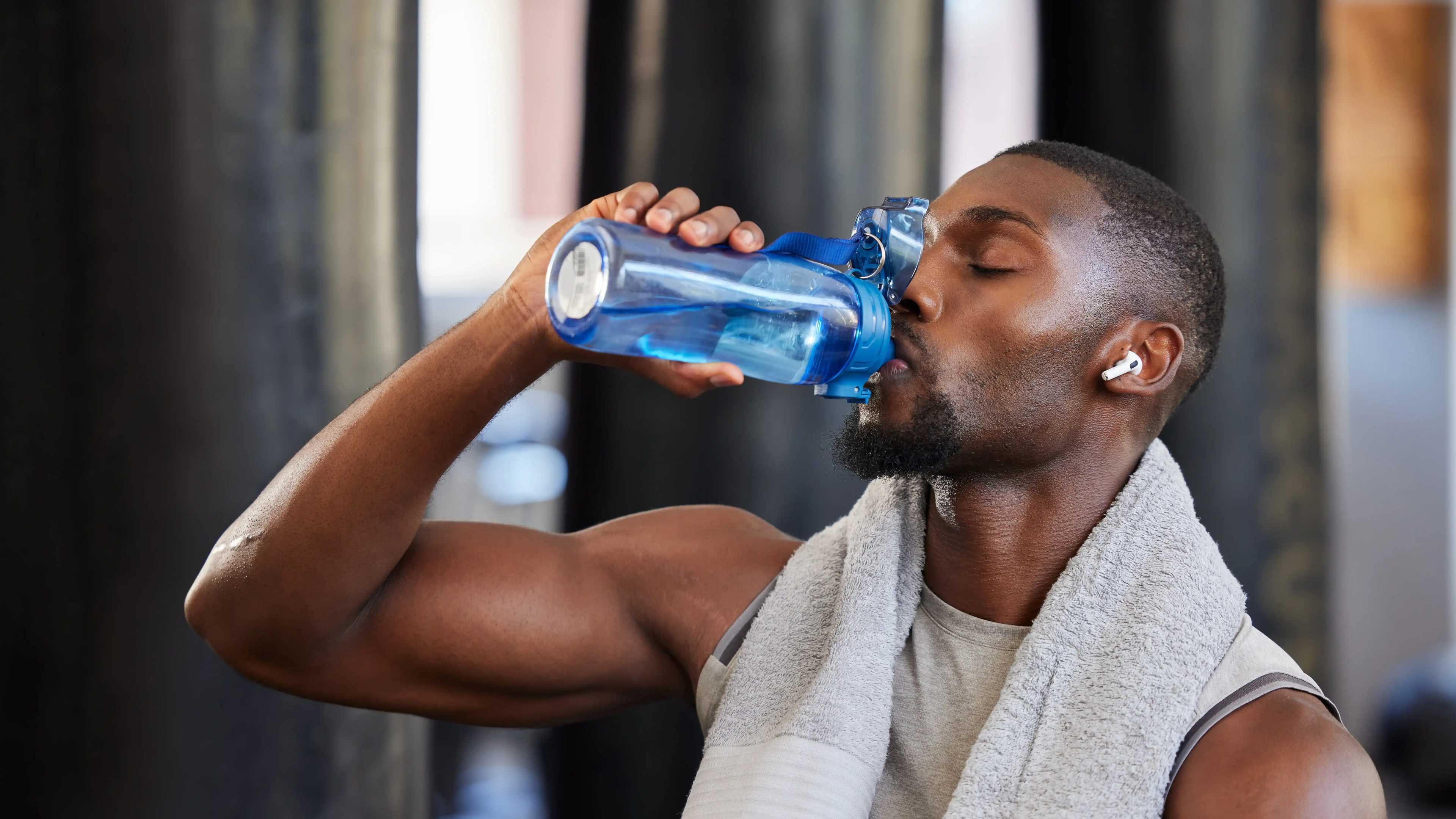 Ein sportlicher Mann trinkt im Fitnessstudio aus einer Wasserflasche