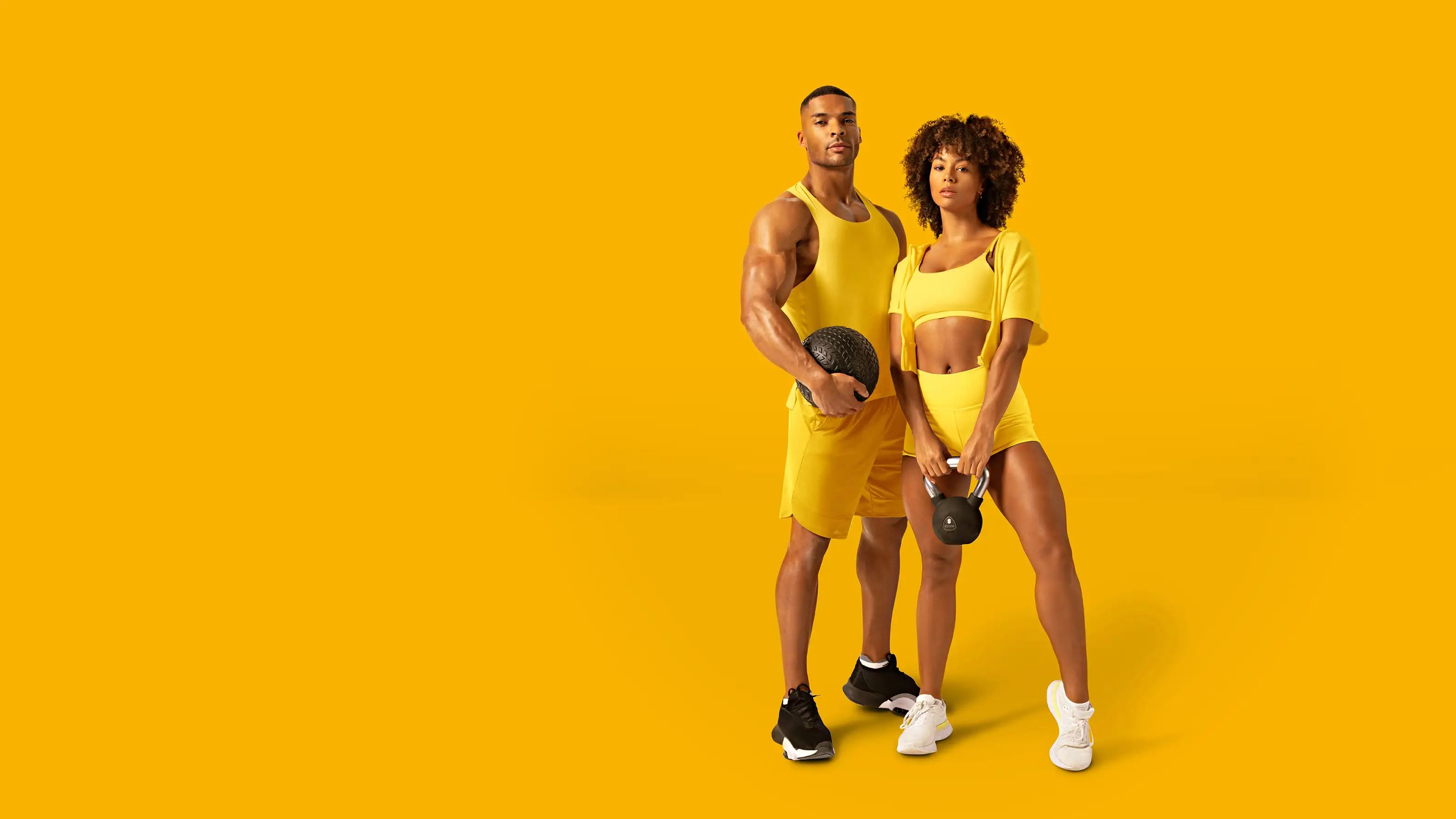 Sportler mit Medizinball und Sportlerin mit Kettlebell in gelber Sportbekleidung